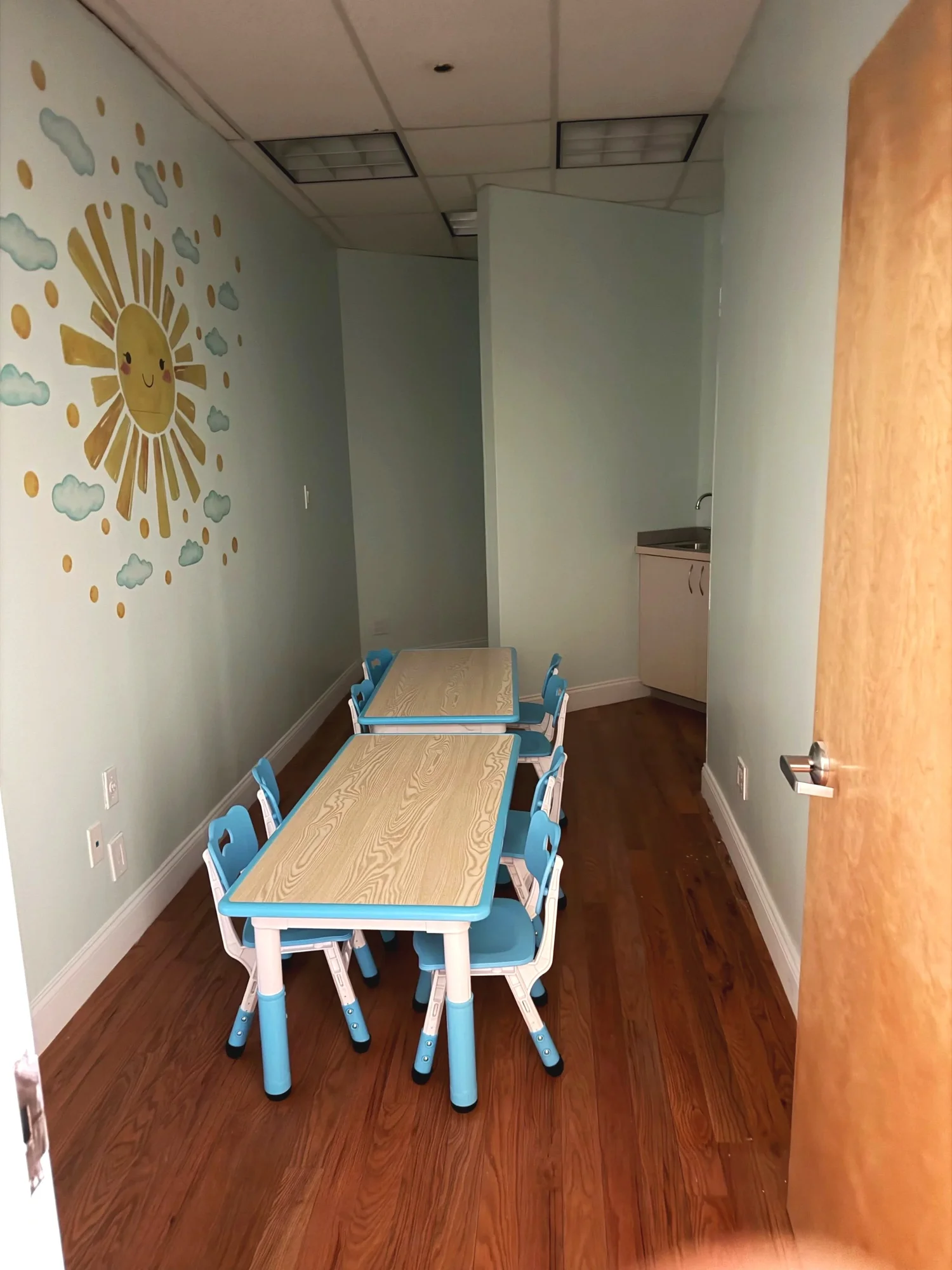 Room with a cheerful painted sun mural and blue chairs at small tables