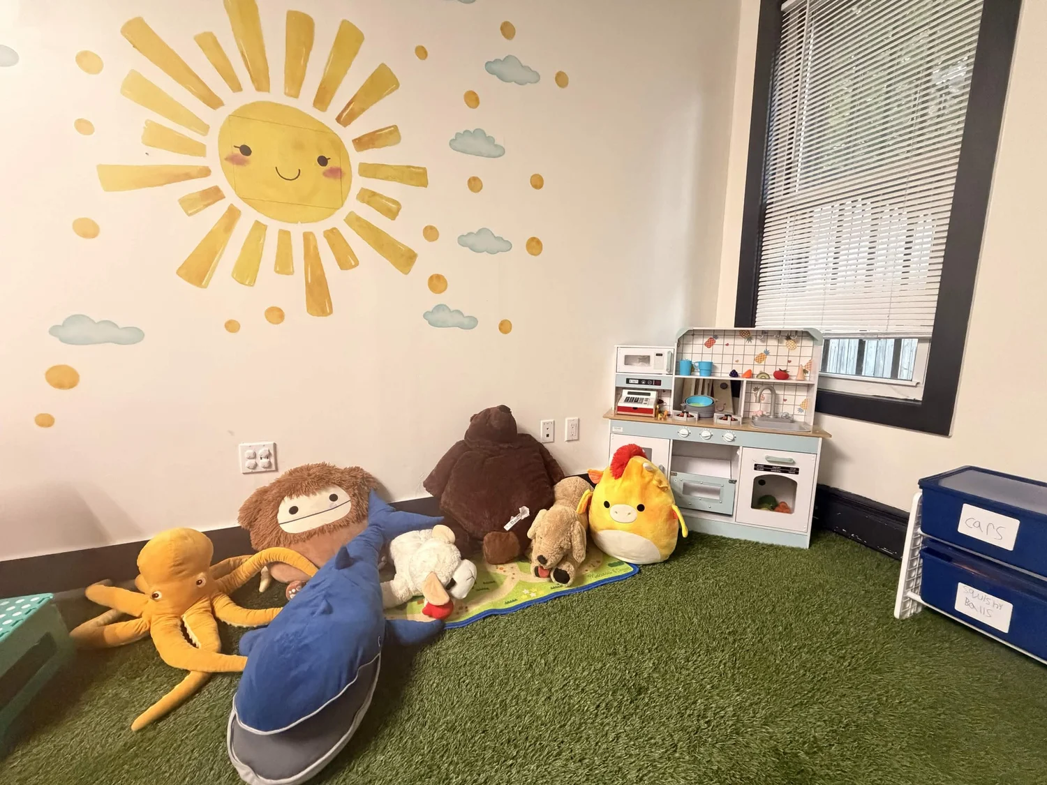 Children's play corner with plush lion, giraffe, and octopus toys on a green carpet