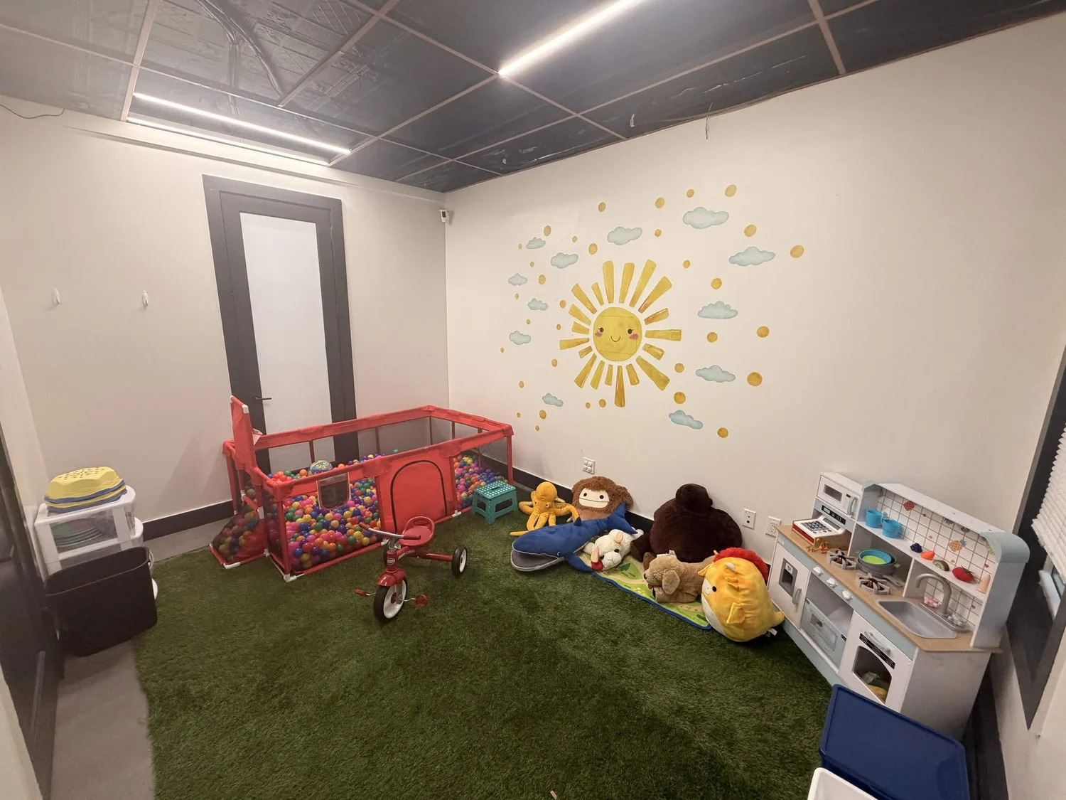 Playroom with a ball pit, toy kitchen, and a smiling sun mural on the wall